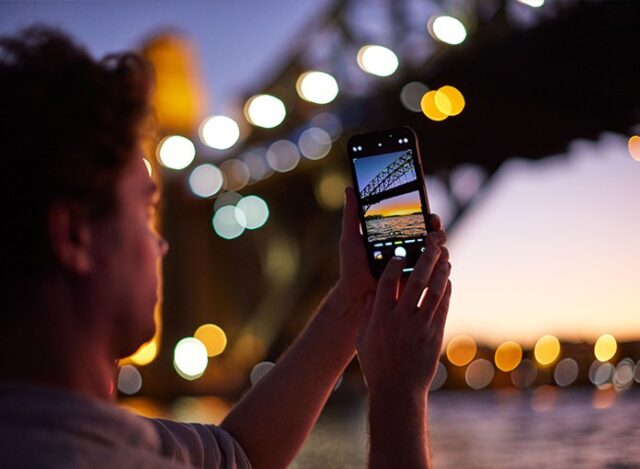 A person is taking pictures below the Sydney Harbour Bridge in the evening.